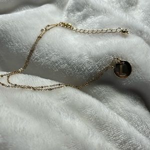 Necklace goldtone with beads along the chain.Pendant is goldtone disc L cut out.